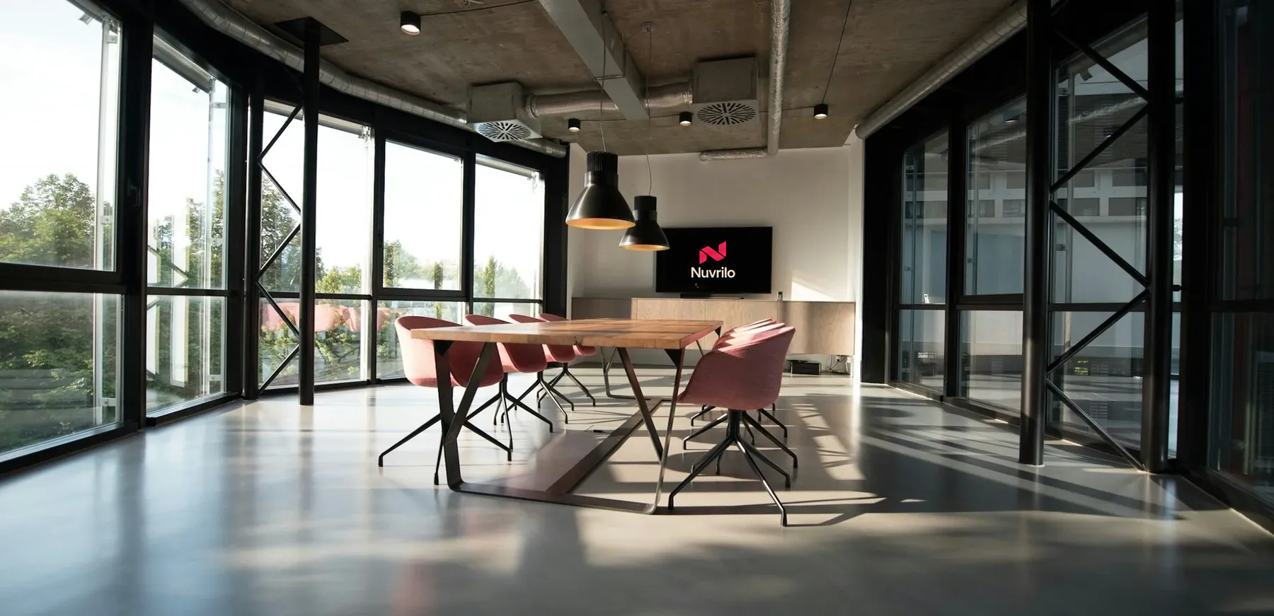 The Nuvrilo studio: a long wood table with pink chairs and the Nuvrilo mark on screen